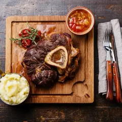 Wołowe ossobuco z puree ziemniaczanym, sosem i gałązką rozmarynu na desce.