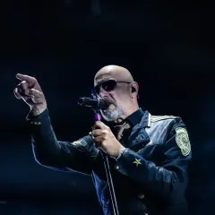 Der Sänger von Eisbrecher Ludwigsburg, mit Sonnenbrille und markanter Jacke, singt ins Mikrofon und zeigt mit dem Finger ins Publikum.