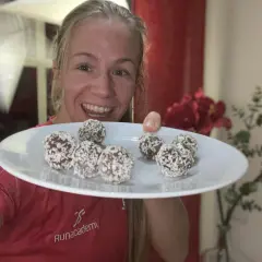 Glad kvinna visar en tallrik med nyttiga chokladbollar täckta av kokos. Perfekt för löpare!
