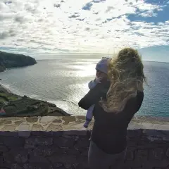 Widok na wybrzeże z małą wioską i oceanem. Kobieta trzyma dziecko, podziwiając krajobraz. Azory czy warto? Tak!