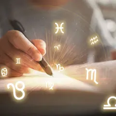 Dłoń pisze piórem, a wokół niej krążą wszystkie znaki zodiaku, tworząc magiczny krąg.