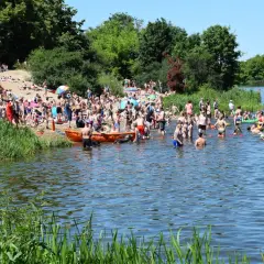 Tłum ludzi na plaży i w wodzie nad Jeziorkiem Czerniakowskim w słoneczny dzień.