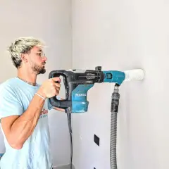 Giovane con trapano Makita crea tracce nel muro senza polvere, aspirando detriti in tempo reale.