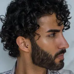 Hombre con un moderno peinado chino, cabello rizado oscuro y barba cuidada.