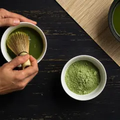 Hände bereiten Matcha zu. Pulver und fertiger Tee auf dunklem Holz. Eine positive matcha tee abnehmen erfahrung beginnt hier.
