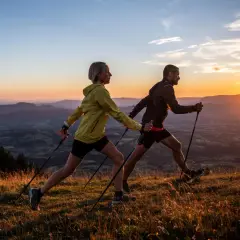 Para uprawiająca nordic walking na tle zachodzącego słońca nad górami.