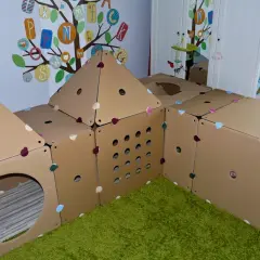 Kreatywne zabawki z kartonu diy tworzą domek do zabawy. Kolorowe serduszka zdobią kartonowe ściany, a otwory zapraszają do eksploracji.