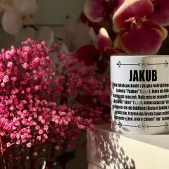 Kubek z napisem "JAKUB" i opisem imienia, otoczony delikatnymi, różowymi kwiatami. Idealny prezent na imieniny Jakuba.
