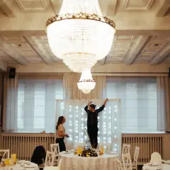 Dwie kobiety przygotowują salę weselną, jedna stoi na drabinie, dekorując tło światełkami. To początek drogi, jak zostać wedding plannerką.