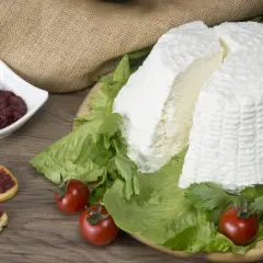 Un grande blocco di ricotta fresca, circondato da lattuga e pomodorini, con bruschette e marmellata in una ciotola. Diversi tipi di ricotta sono presentati in modo invitante.