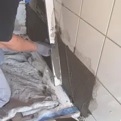 Hand mit Handschuh trägt Mörtel auf alte Fliesen auf, um eine Abdichtung zu schaffen.