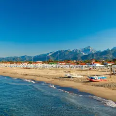 Słoneczna plaża w Toskanii, z rzędami białych parasoli i leżaków, w tle góry i błękitne morze.