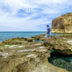 Hombre contempla el mar azul desde las rocas cerca del faro de Cabo de Gata. Acantilados y aguas cristalinas.