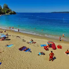 Gente disfrutando del sol y el mar en la playa Portocelo. Arena dorada, aguas turquesas y un día perfecto para relajarse.