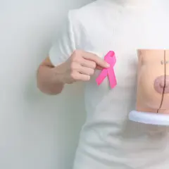 Dłoń trzyma różową wstążkę obok modelu piersi, symbolizując nadzieję po mastektomii z rekonstrukcją.