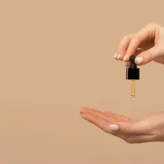 Una mano sostiene un gotero con aceite de jojoba para el pelo, listo para aplicarlo en la otra mano.
