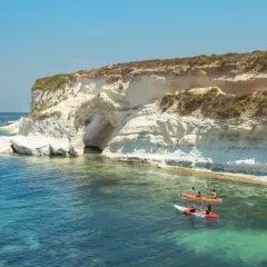 Malta w październiku: kajaki pływają przy klifach z jaskinią. Słońce i turkusowa woda zachęcają do aktywnego wypoczynku.