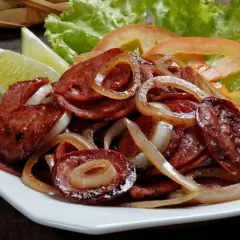 Pyszna kiełbasa smażona z cebulą, podana z sałatą, pomidorem i limonką. Idealna na szybki obiad.