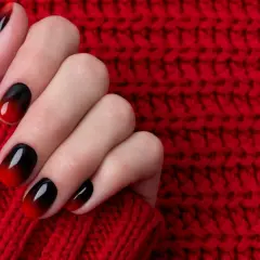 Dłoń z paznokciami w stylu ombre, od czerni do czerwieni. Idealny przykład, jak zrobić ombre na paznokciach.