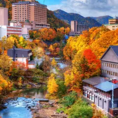 Town nestled in a valley with a river, surrounded by trees in vibrant autumn colors.