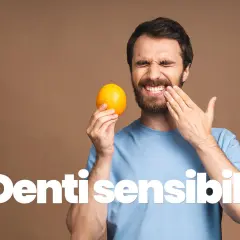 Uomo con espressione di dolore, tiene un'arancia e si tocca la guancia, soffre di sensibilità dentale.