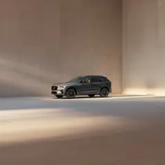 En mörkgrå Volvo XC60 står i ett ljust, minimalistiskt rum. Bilen visar upp sina eleganta linjer och fälgar, en perfekt representation av Volvo utrustningsnivåer.