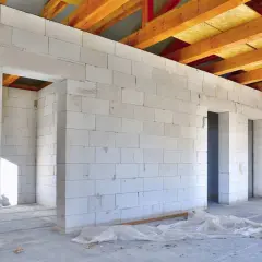 Budowa domu z białych bloczków z betonu komórkowego, widoczne drewniane belki stropowe.