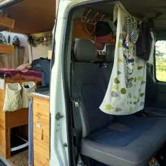 Aménagement d'un van pour 4 : lit, rangements en bois, sièges et rideau décoratif.