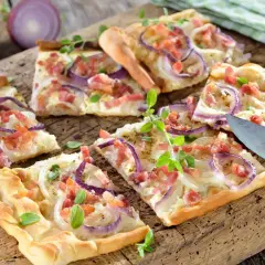 Co zrobić z ciasta na pizzę? Pyszny placek z cebulą i boczkiem, pokrojony na desce, gotowy do podania.
