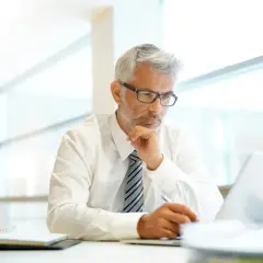 Uomo d'affari con occhiali riflette sul suo lavoro, forse calcolando lo scorporo IVA al 10% per un nuovo progetto.