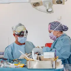 Två kirurger arbetar med instrument på ett bord. En av dem har en lampa på huvudet, vilket kan tyda på en komplicerad operation, kanske efter ett ansiktslyft.