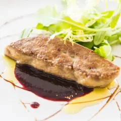 Un morceau de foie gras poêlé, servi avec une sauce aux fruits rouges et une salade verte. Une recette raffinée pour un plat d'exception.
