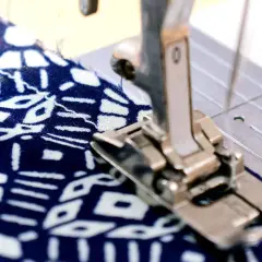 Sewing machine foot creating a narrow hem on a blue and white patterned fabric.