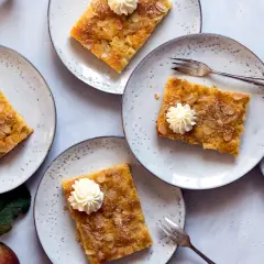 Saftiger Apfelkuchen vom Blech, garniert mit Sahnetuffs und Mandelblättchen, auf Tellern angerichtet.