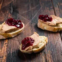 Trois toasts de pain de campagne garnis de foie gras et de confiture de fruits rouges. Un délice qui évoque le foie gras origine.