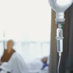 Kroplówka dożylna, symbol nadziei i walki z chorobą. W tle niewyraźna postać pacjenta, który przechodzi chemioterapię.