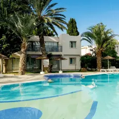 Basen w hotelu Leptos Paphos Gardens Holiday Resort, otoczony palmami i zielenią, zaprasza na relaks.