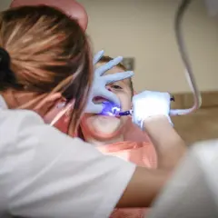 Dentysta z niebieskim światłem bada zęby dziecka.