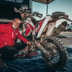 Uomo in giacca rossa vicino a moto da cross sporca, pronto a capire come pulire il motore dopo una gara.