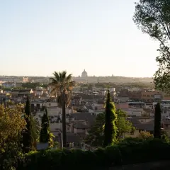 Panoramic view of Rome with St. Peter's Basilica dome in the distance, framed by trees and greenery.