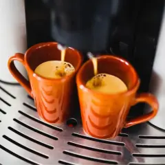 Dwa pomarańczowe kubeczki wypełniają się aromatycznym espresso. Idealny poranek z kawą.