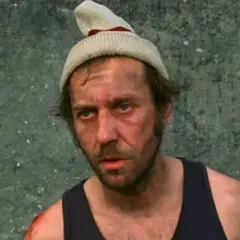 Brudny mężczyzna w czapce i podkoszulku, z raną na ramieniu. Widać, że pieniądze to nie wszystko, obsada filmu.