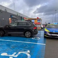 Czarny SUV zaparkowany na niebieskim miejscu dla niepełnosprawnych, obok radiowóz policyjny. To pytanie o to, jak długo można parkować na miejscu dla niepełnosprawnych, jest tu bardzo aktualne.