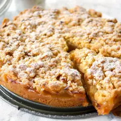 Saftiger apfelkuchen mit streusel, bestäubt mit Puderzucker. Ein Stück wurde bereits herausgenommen.