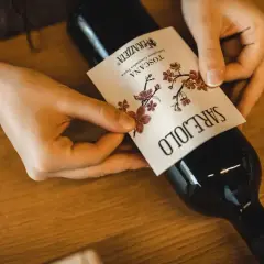 Mani che applicano l'etichetta a una bottiglia di vino rosso, forse il best wine in Tuscany.