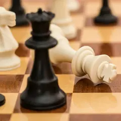 Szachownica z leżącym białym królem, czarną hetmanką i białym skoczkiem.
