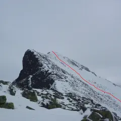 Snöklädda bergstoppar med en röd markerad led som leder uppåt. En utmanande sylarna topptur i vinterlandskap.