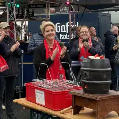 Menschen mit roten Schals klatschen bei Ruppichteroth Veranstaltungen. Eine Frau mit blonden Haaren steht im Mittelpunkt, daneben ein Mann mit Mikrofon.