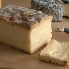 Un pezzo di taleggio dal sapore intenso, con una fetta tagliata e altri formaggi sullo sfondo.