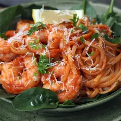 En skål med pasta pomodoro med räkor, toppad med riven ost och färsk persilja. En citronklyfta vilar ovanpå.